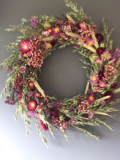 a wreath with pink flowers and green leaves hanging on the wall next to a gray wall