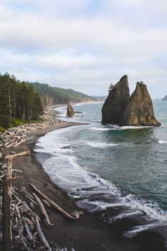 the beach is lined with driftwood and large rock formations on either side of the water