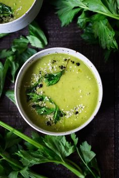 two white bowls filled with green soup and garnished with parsley