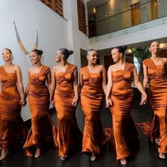 a group of women standing next to each other in orange dresses on a black floor