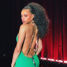 a woman in a green dress standing next to a red curtain