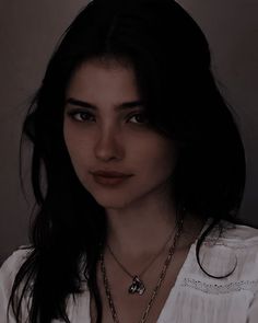 a woman with long black hair wearing a white shirt and holding a silver chain around her neck