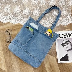 a denim bag sitting on top of a wooden floor next to a pair of glasses