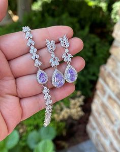 a person holding three different pieces of jewelry in their hand, one is purple and the other is white