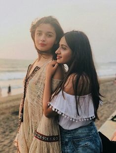 two young women standing next to each other near the ocean