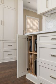 an open cabinet in the middle of a kitchen with white cabinets and wood flooring