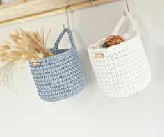 two crocheted baskets hanging from hooks on a wall with dried plants in them