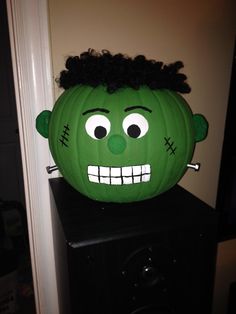 a green pumpkin with a creepy face on top of it's head sitting on a black shelf