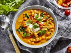 a white bowl filled with soup next to a spoon and some lettuce on the side