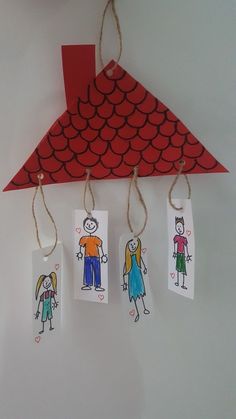 three children's drawings are hanging from twine strings on a red paper hanger