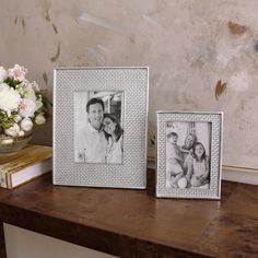 two frames sitting on top of a wooden table next to a vase filled with flowers