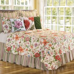 a bed with floral comforter and pillows on top of it in front of large windows