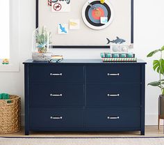 a blue dresser in a white room with pictures on the wall and plants next to it