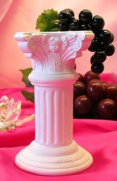 a white vase sitting on top of a table next to grapes and other items in the background