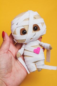 a hand holding a small stuffed animal wrapped in bandages with a pink heart on it