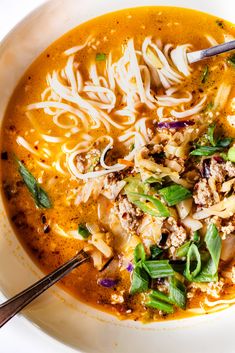 a bowl of soup with noodles, meat and veggies in it on a white surface