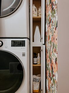 a white washer and dryer sitting next to each other in a room with floral wallpaper