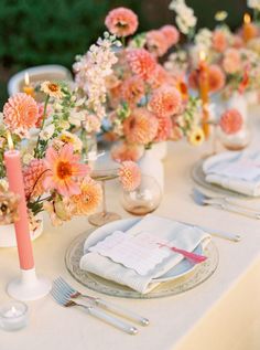 the table is set with pink and white flowers in vases, silverware, and napkins