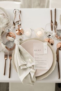 a place setting with silverware, napkins and candles on a white table cloth