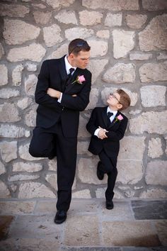 two young boys in tuxedos leaning against a stone wall