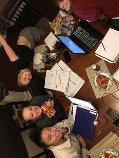 four people sitting at a table with pizza and notebooks in front of their faces