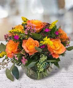 a vase filled with orange and pink flowers on top of a wooden table next to greenery