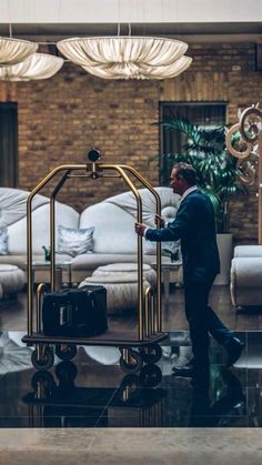 a man in a suit pushing a luggage cart through a living room filled with couches