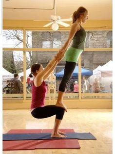 two women doing yoga poses in an open room with large windows and people looking out the window