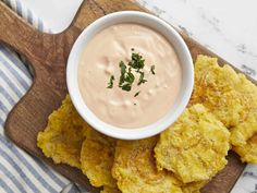 a wooden cutting board topped with tater tots covered in ranch dip and garnished with parsley