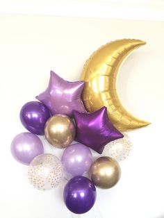 purple and gold balloons are arranged in front of the moon