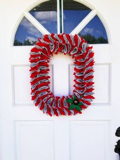 a red and white wreath hanging on the front door of a house with a black dog sitting next to it