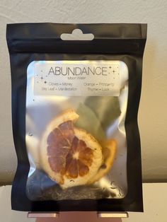 an orange is in a black bag on a counter top, with the label above it that says abundance