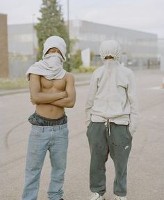 two shirtless men standing in the street with their arms crossed and looking at each other