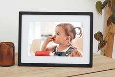 a photo frame sitting on top of a wooden table next to a candle and potted plant