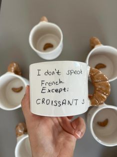 someone is holding up a coffee mug with words written on it in front of some cups