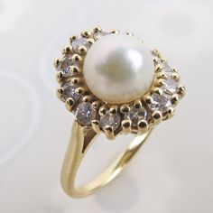 "A lovely natural white pearl tops this elegant 14k yellow gold diamond halo ring. The white lustrous pearl sits 7/16 inch tall above the finger. A row of twelve tiered 2mm .03 carat diamonds flow around the pearl. The dazzling gemstones top a linear wire gallery and smooth sturdy band.  The inside is stamped \"14k\" (gold purity) with no other identifying hallmarks. The ring has an estimated total weight of .36 carat diamonds.  The ring measures an approx. petite size 4.75 and could be re-sized Luxury Formal Pearl Ring With Halo Design, Timeless Diamond Pearl Ring With Center Stone, Timeless Diamond Pearl Ring With Prong Setting, Timeless Pearl Ring With Diamond Accents, Diamond White Pearl Ring With Diamond Accents, Classic Pear-shaped Diamond White Diamond Ring, Classic Cluster Halo Wedding Ring, Timeless Diamond-white Pearl Ring With Diamond Accents, Classic Pearl Ring With Prong Setting In Diamond White