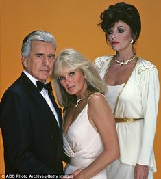 two women and a man in formal wear posing for a photo with an orange background