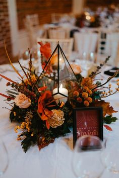 an arrangement of flowers and candles on top of a white table cloth with a candle