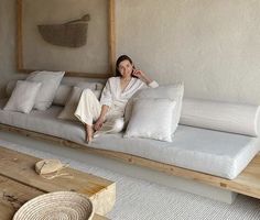 a woman sitting on top of a white couch in a living room next to pillows