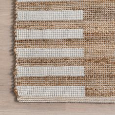 a woven rug with white and brown stripes on top of a wooden flooring surface