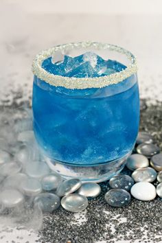 a blue cocktail sitting on top of a table next to rocks and pebbles in front of it