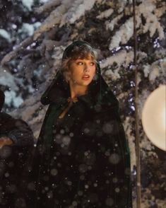 a woman standing in the snow wearing a green cloak