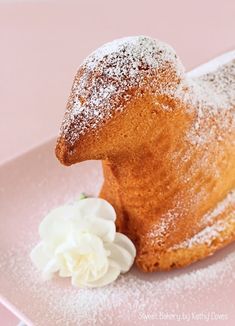 a powdered sugar coated pastry on a pink plate with a flower in the foreground