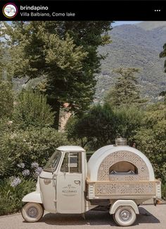 an old truck is parked in front of some trees and bushes with a pizza oven on the back