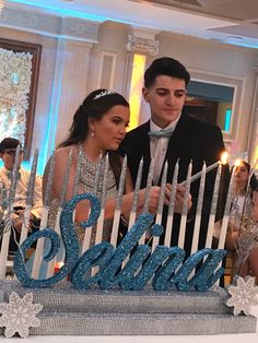 a young man and woman standing in front of a cake with candles that spell out the word santa