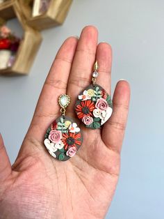 the hand is holding two earrings with flowers on them