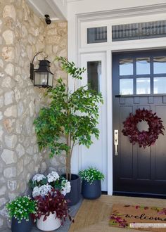 three potted plants are sitting on the front porch next to a door with a wreath