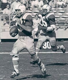 an old photo of two football players running on the field with people in the stands watching