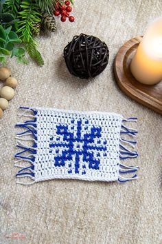 a knitted placemat with blue and white designs on it next to a lit candle