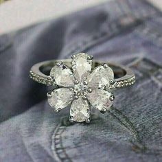 a white flower ring sitting on top of a pair of blue jeans with diamonds in the middle